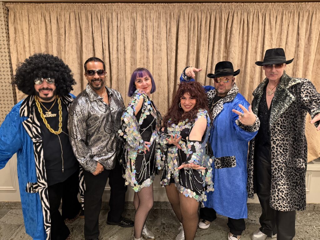 Six people in glittery 1970s disco costumes